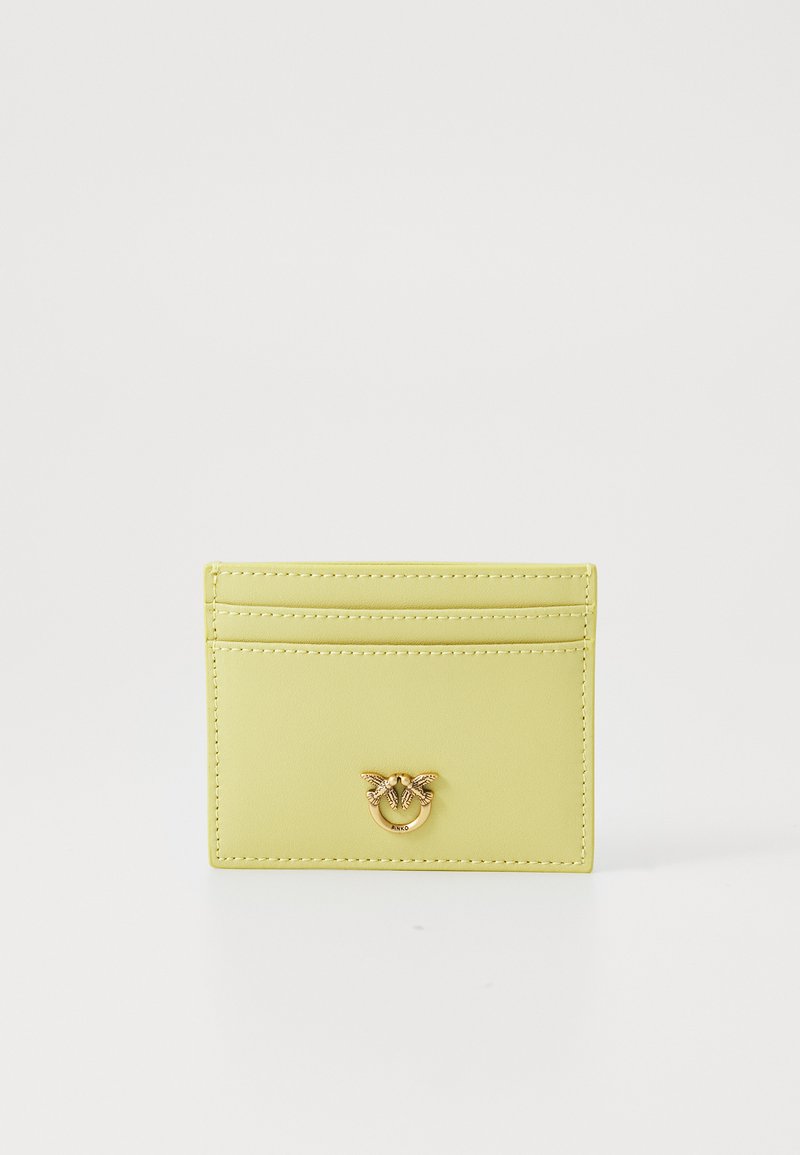 Geltona odinė kortelių laikiklis su auksinės spalvos detalėmis. Turi šešis kortelių lizdus ir centrinį emblemos dizainą. Lygus paviršius su siuvinėtomis kraštinėmis.