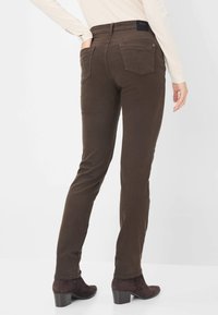 Bruine denim skinny jeans met een middenhoog taille, vijf zakken en een subtiele textuur. Draagt met donkere hak enkellaarsjes.
