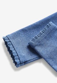 Tessuto in denim blu con una finitura testurizzata, caratterizzato da un orlo arricciato e bordi morbidi e piegati. Il materiale appare flessibile e informale.
