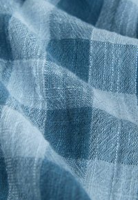 Blåt og lyseblåt ternet stof med en struktureret vævning, der viser rynker, som fremhæver det bløde materiale og det tydelige mønster.