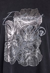 Camiseta de tela oscura con un diseño floral metálico en plata, con líneas intrincadas y texturas detalladas, acompañada de un texto estilizado.