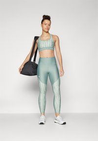 Sostén deportivo y leggings en verde menta con un patrón texturizado. Los leggings presentan un diseño de bloques de color, combinados con una mochila de gimnasio negra.