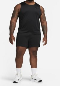 Camiseta sin mangas negra de Nike y pantalones cortos negros, con un diseño ajustado. Logo blanco de Nike en el pecho. Zapatillas blancas con detalles negros.