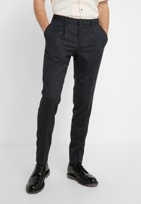 Szare spodnie o dopasowanym kroju, wykonane z gładkiego materiału, z płaskim przodem, bocznymi kieszeniami i slim fit. Uzupełnione o wypolerowane czarne buty.