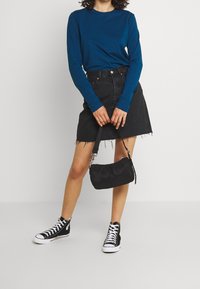 Long-sleeve teal shirt, black denim skirt with frayed hem, black crossbody bag, and black high-top sneakers with white laces.