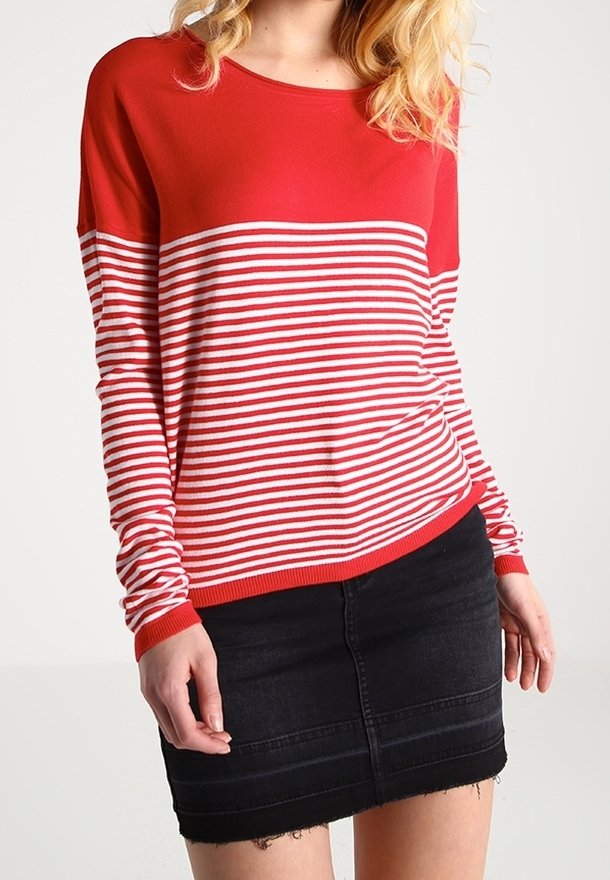 Femme portant un pull à manches longues rayé rouge et blanc et une mini-jupe en jean noire avec un ourlet effiloché.