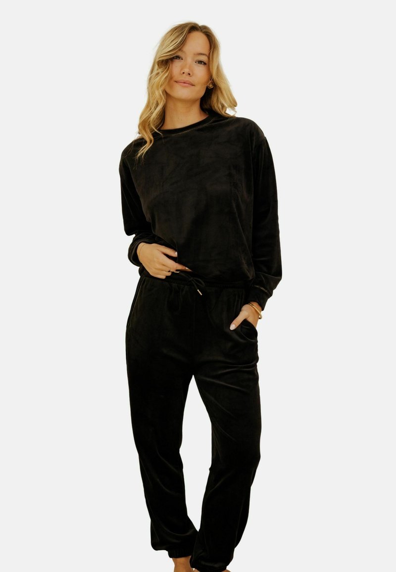 Ensemble de loungewear en velours noir comprenant un haut à manches longues et un pantalon de jogging avec des poignets élastiques et une taille à cordon de serrage; texture douce, coupe décontractée.