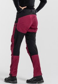 Men's outdoor pants in black with maroon accents. Features zippered pockets, adjustable cuffs, and a relaxed fit design. Textured fabric.
