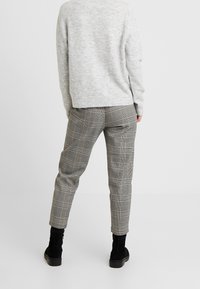 Grauer Pullover über kariertem, grauem und schwarzem Hose, die schmal zuläuft und ein Muster aus dünnen und dicken Linien aufweist, kombiniert mit schwarzen Knöchelboots.