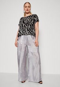 Haut à rayures zèbre noir et blanc avec des manches courtes, associé à un pantalon argenté large et brillant. Des talons ouverts noirs complètent la tenue.
