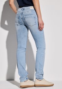 Jeans ajustados de color azul claro, hechos de denim, con una cintura de altura media, bolsillos traseros y un sutil desvanecido, combinados con zapatillas de deporte beige con textura.