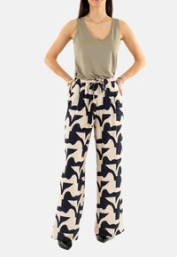 Top de tirantes verde oliva con escote en V y purpurina, combinado con pantalones holgados de tiro alto que presentan un patrón abstracto en azul marino sobre un fondo beige.