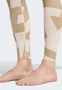 Beige leggings with abstract light and dark patterns, fitted design, soft texture, and clear stitching along ankles, worn with bare feet.