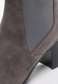 Stivaletto ankle in suede grigio con pannello elastico testurizzato, tacco impilato e cuciture a contrasto lungo la cucitura. Design moderno con linee eleganti.
