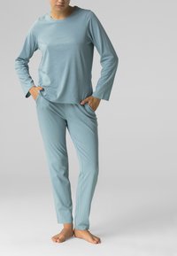 Jasnoniebieska bluzka z długim rękawem oraz pasujące spodnie, wykonane z miękkiego materiału. Strój ma luźny krój i boczne kieszenie w spodniach.