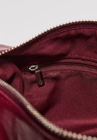 Innenraum einer burgunderroten Stofftasche mit sichtbarem silberfarbenem Reißverschluss und einer kleinen Innentasche. Weiche Textur mit sauberem, glattem Finish.