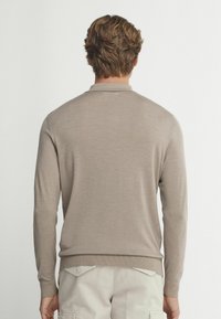 Beige stickad tröja med långa ärmar och polo-krage, med en slät textur och ribbade muddar och fåll. Inga synliga mönster eller hårdvara.