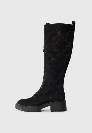 Bottes noires hautes en suède avec un motif découpé à carreaux, un laçage à l'avant et une semelle épaisse et texturée.