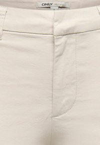 Pantalon en coton beige clair avec une texture lisse, doté d'une poche avant, d'une coupe droite et de coutures discrètes au niveau des coutures.