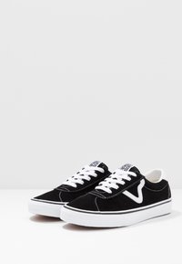 Sorte semskede sneakers med hvite lisser og gummisåler. Har en hvit logo på siden og hvite sømdetaljer. Klassisk lavt design.