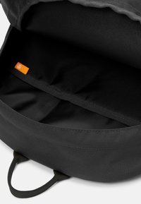 Musta reppu, jonka sisäpuolella on tasainen vuori, oranssi etiketti ja sileä pinta. Sisältää yhden osaston ja kaksinkertaiset sivukahvat.