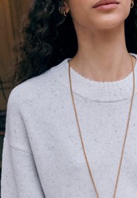 Pullover sweater in light gray knit with a ribbed neckline, featuring subtle speckles. A thin gold chain necklace is visible.