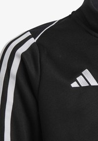 Zwarte sportjacket met hoge kraag, textuurstof en witte gestreepte accenten op de schouders. Adidas-logo in witte borduursel.