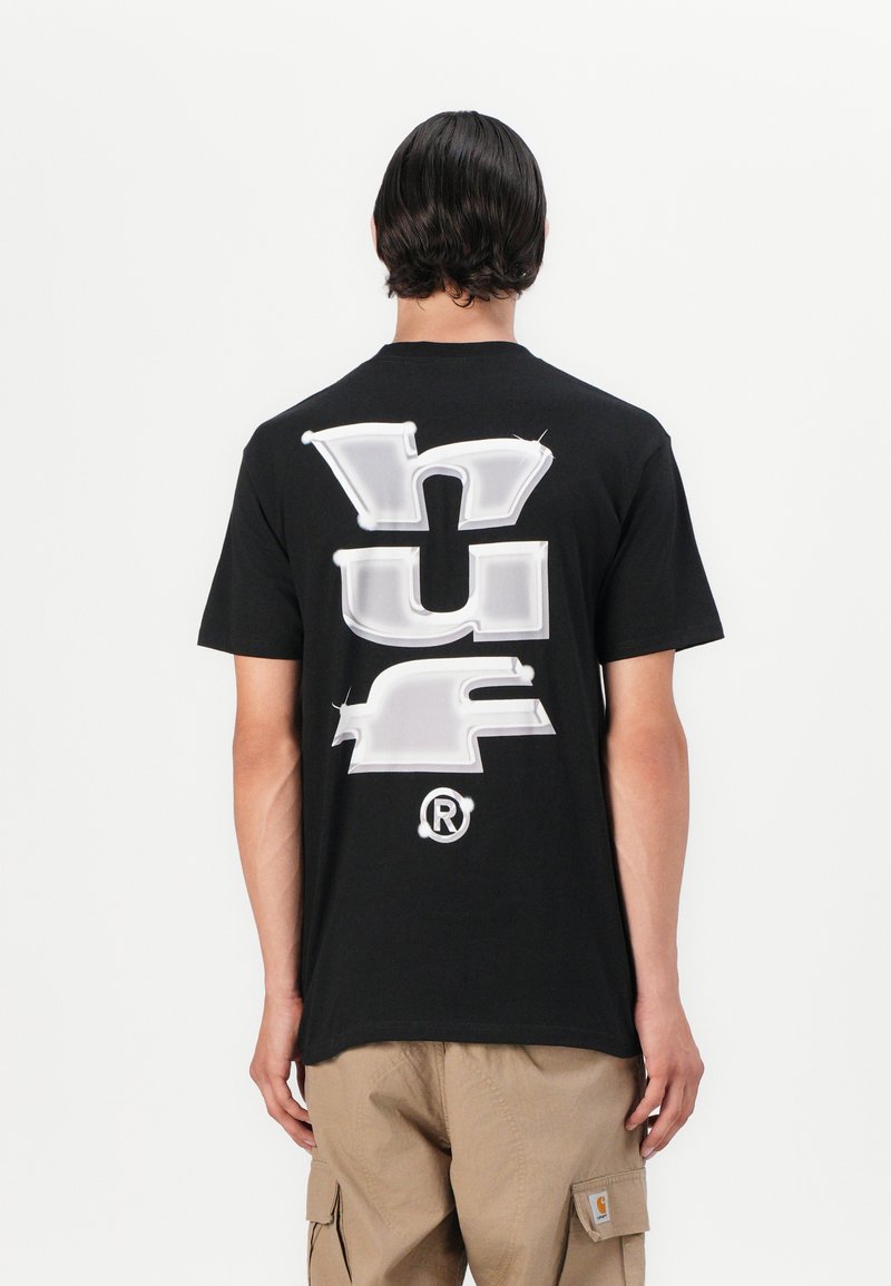 Sort bomulds T-shirt med et stort hvidt grafisk tryk, der står "HUF" i fed skrift på ryggen, rund logo detalje i bunden.