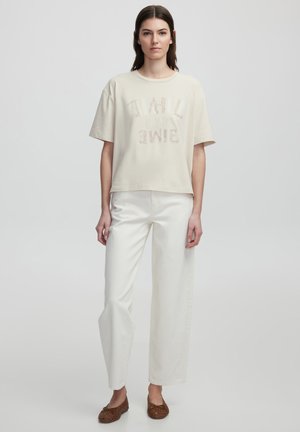 Beige crop t-shirt met textuurlettering, gecombineerd met hoog-getailleerde witte broeken en bruin gevlochten instappers. Gladde stofafwerking.