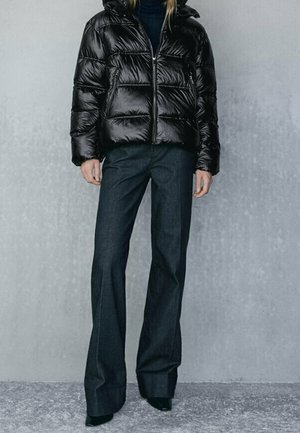 Black padded puffer jacket with a shiny finish and hood, paired with dark wide-leg trousers. Smooth texture with a sleek design.