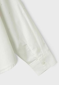 Lichtgele blouse met lange mouwen van een gladde stof, voorzien van subtiele zilveren stippen en een knoopmanchet.