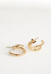 Goldfarbene Creolen, entworfen mit glatten, runden Formen und einer glänzenden Oberfläche; verfügen über einen Stecker für einen sicheren Halt.