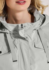 Hellgraue Kapuzenjacke mit Reißverschluss vorne, verstellbaren Kordeln und Druckknopfpatten-Taschen. Glattes, wasserabweisendes Material.