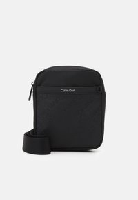 Borsa a tracolla nera con superficie testurizzata e motivo a logo ripetuto. Chiusura con cerniera e tracolla regolabile. Design minimalista.