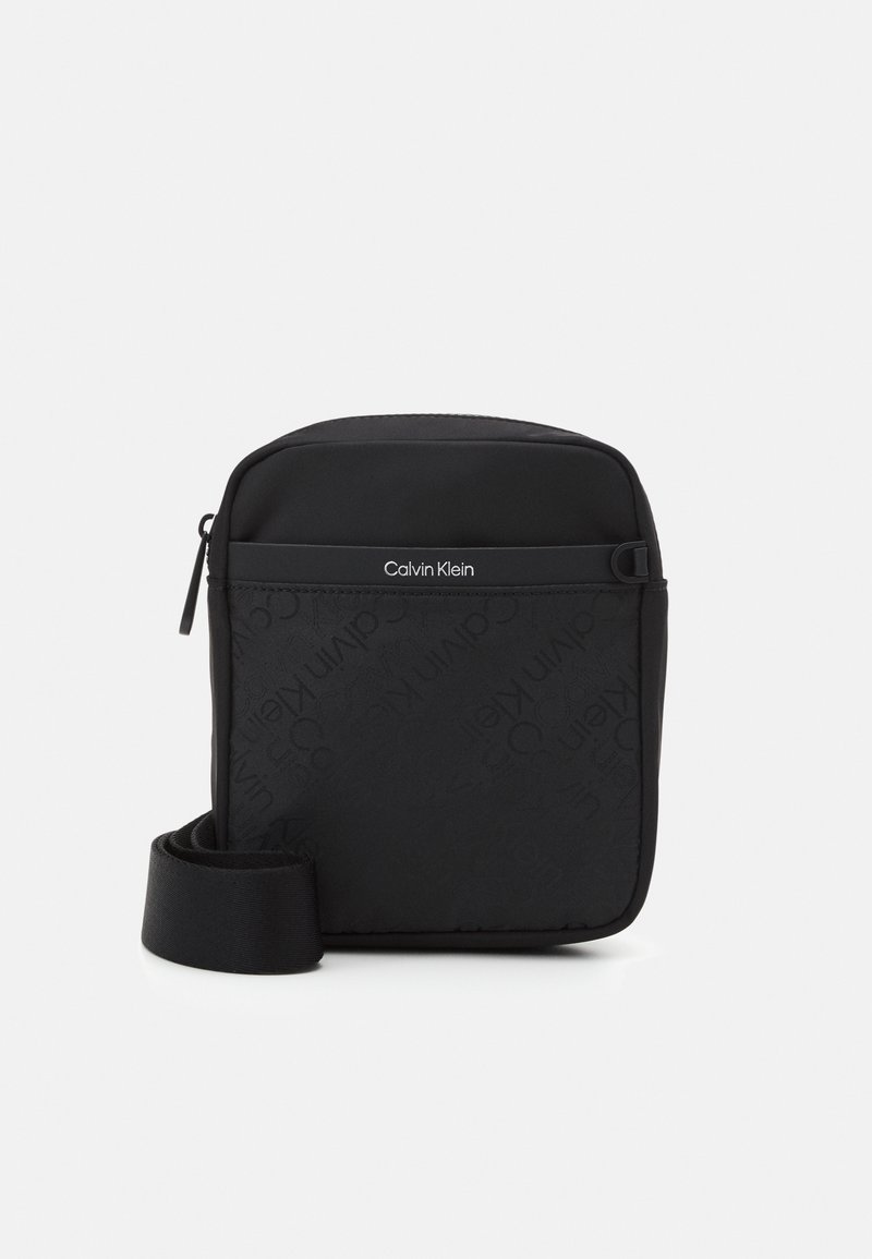 Borsa a tracolla nera con superficie testurizzata e motivo a logo ripetuto. Chiusura con cerniera e tracolla regolabile. Design minimalista.