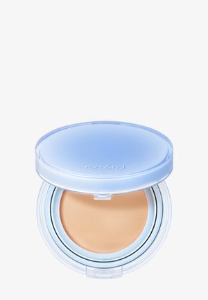Fond de teint compact avec un couvercle translucide bleu clair partiellement ouvert, montrant un maquillage beige à l'intérieur et le nom de la marque "rom&nd" sur le couvercle.