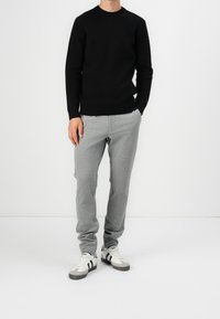 Maglione nero a maglia con collo rotondo, abbinato a pantaloni grigi a righe sottili e sneakers bianche con accenti neri.