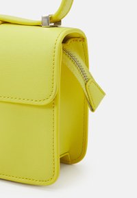 Geel faux leren handtas met een klep sluiting, voorzien van een zilveren ritsdetail en een gladde textuur. Compacter rechthoekige vorm.