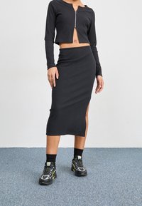 Svart ribbad tvådelad set som består av en crop top med dragkedja och en högmidjad pennkjol med en sidoklyfta; matchad med svarta sneakers.