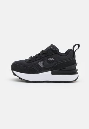 Czarno-białe sportowe buty Nike z cholewką z siatki i zamszu, grubą białą podeszwą, czarnym wsparciem pięty i pętelką z tyłu.