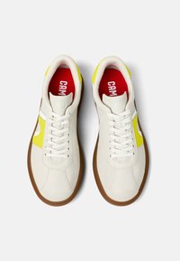 Weiße Leder Sneaker mit einem gelben Akzent, brauner Gummisohle und rotem Innensohle mit "CAMPER"-Logo, strukturiertem Obermaterial und Schnürverschluss.