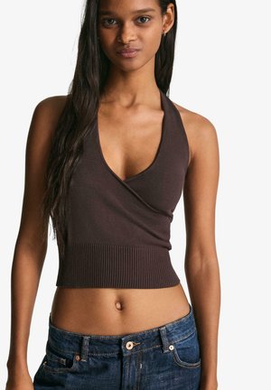 Brązowy top na szyję z żebrowanej tkaniny z głębokim dekoltem w kształcie litery V i dopasowanym żebrowanym dołem. W zestawie z niebieskimi jeansami.