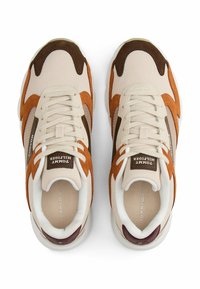 Baskets beiges et orange en matériaux mesh et daim, avec une épaisse semelle blanche et des accents marron contrastants. Comportent un système de laçage et un logo.