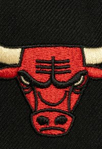 Red embroidered bull logo with black outline on a black textured fabric background. Features curved horns and facial details.