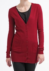 Roter langärmeliger Cardigan mit V-Ausschnitt, vorderen Knöpfen und zwei vorderen Taschen. Hergestellt aus weichem Material mit gerippter Textur.