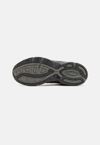 Semelle de chaussure de sport noire et grise avec un caoutchouc texturé, motifs circulaires et angulaires ; dispose d'une semelle durable pour une adhérence et une stabilité optimales.