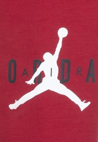 La tela roja presenta una gran silueta blanca de un jugador de baloncesto en el aire, acompañada de texto negro que dice "OADRA."
