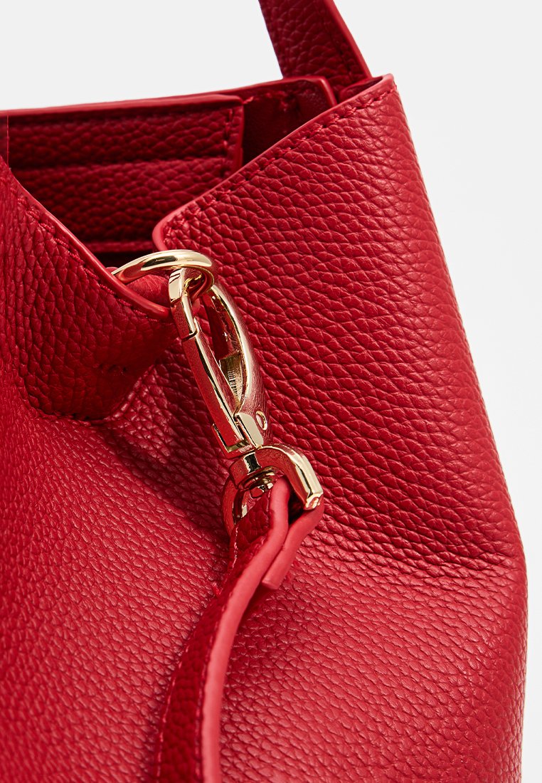 Sac en cuir texturé rouge avec un fermoir en métal doré et un design élégant. Le tissu semble souple avec une finition en cuir grainé.