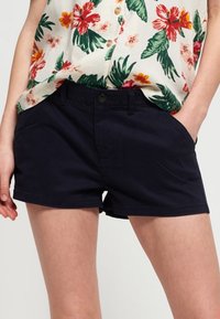 Marinblå bomullsshorts med sidfickor och knäppning framtill. Tyget ser slätt ut med en strukturerad passform och snygg fåll.