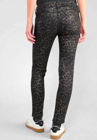 Svarta jeans med ett mönster av leopardtryck, åtsittande stil, fem fickor och ankellängd, kombinerat med vita sneakers. Strukturerad tygfinish.